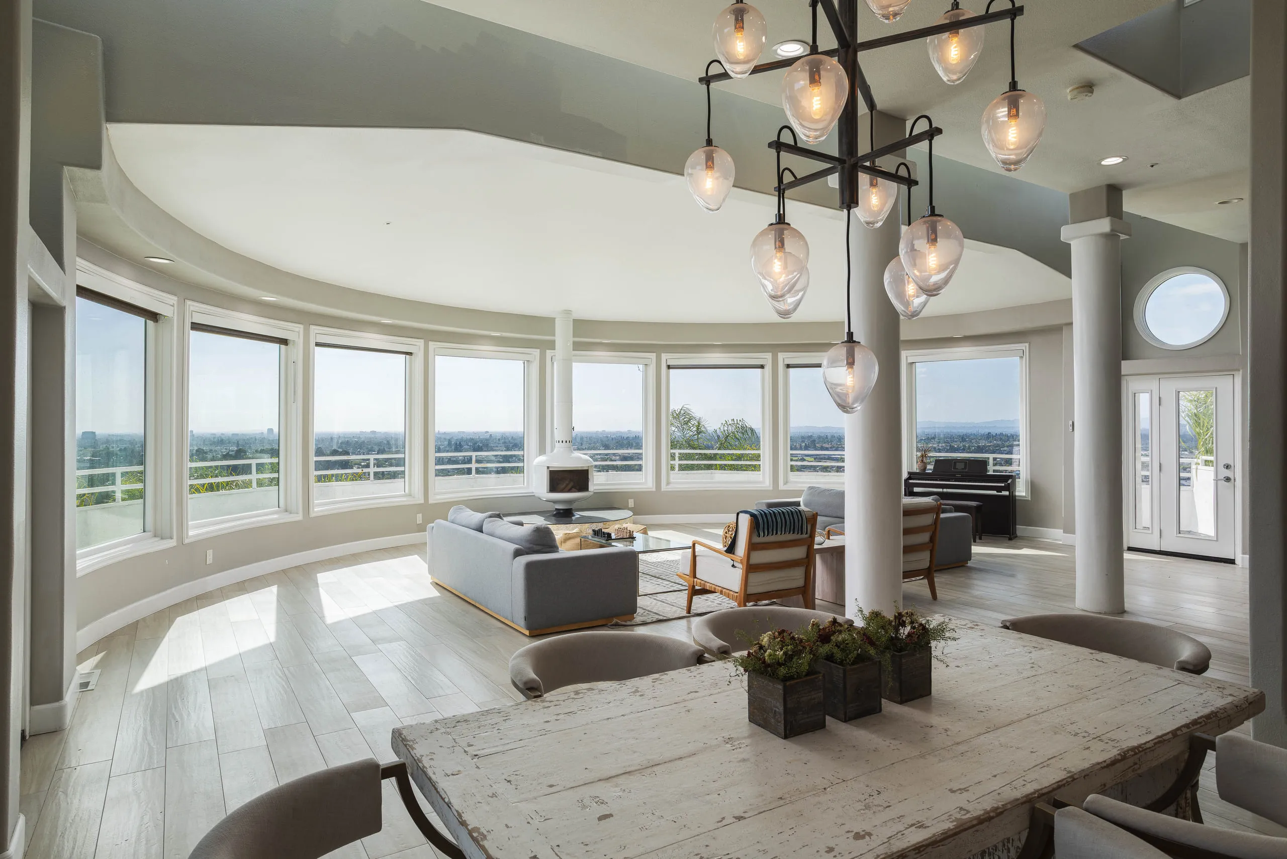 The curved great room — panoramic windows and the dining table beneath a glass chandelier